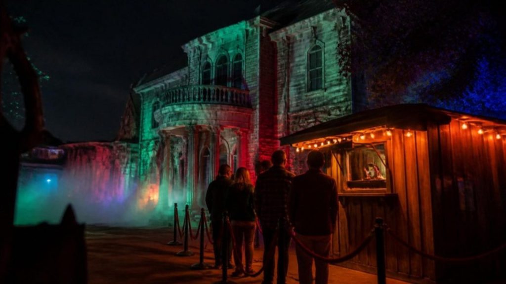 Guests lined up outside a fog-filled haunted house attraction lit in eerie green and red at night